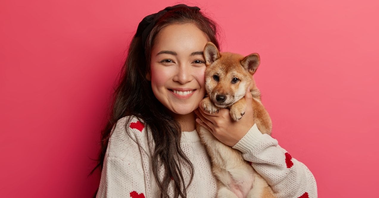 Smiling woman holding a puppy against a pink background