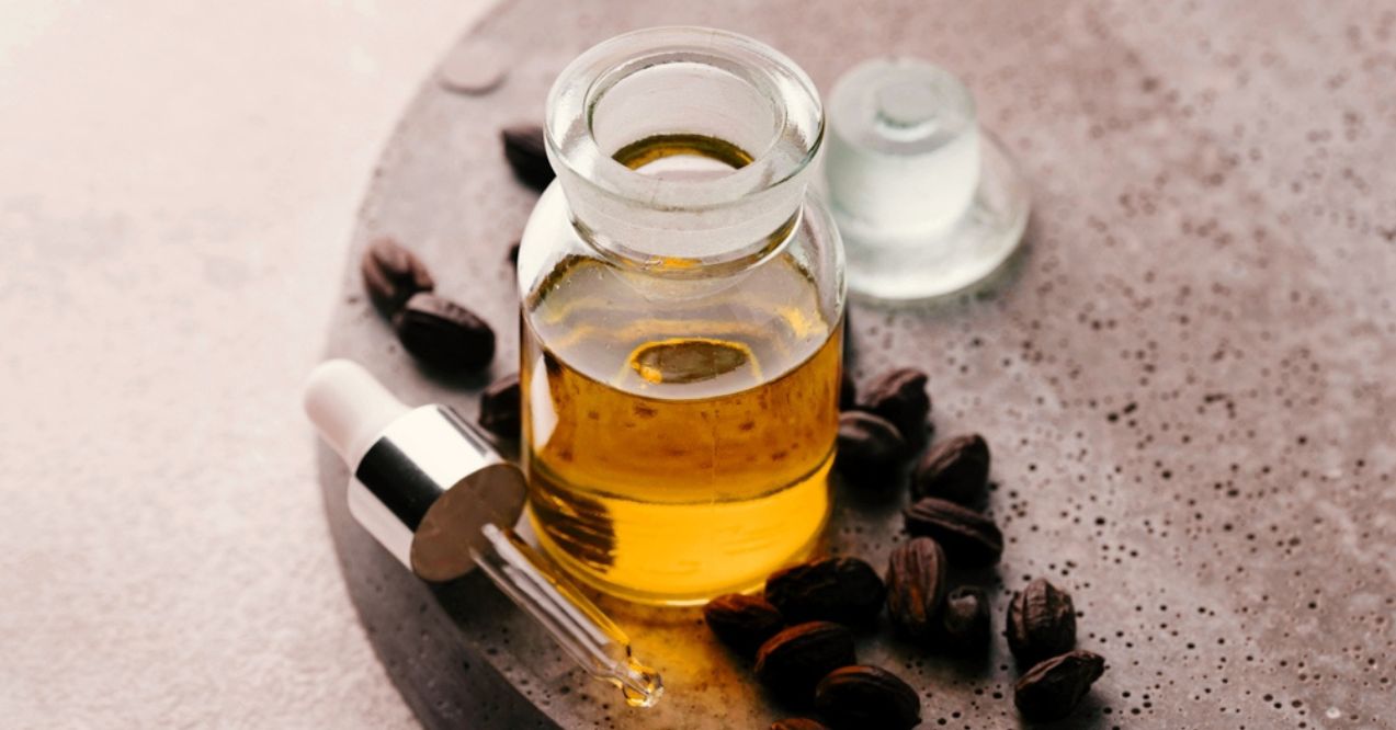 Glass bottle of jojoba oil with dropper and seeds on a textured surface