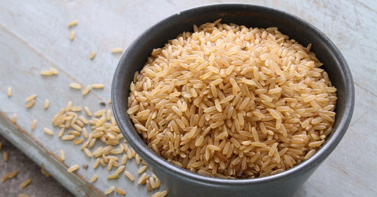 Bowl of uncooked brown rice with some grains scattered around