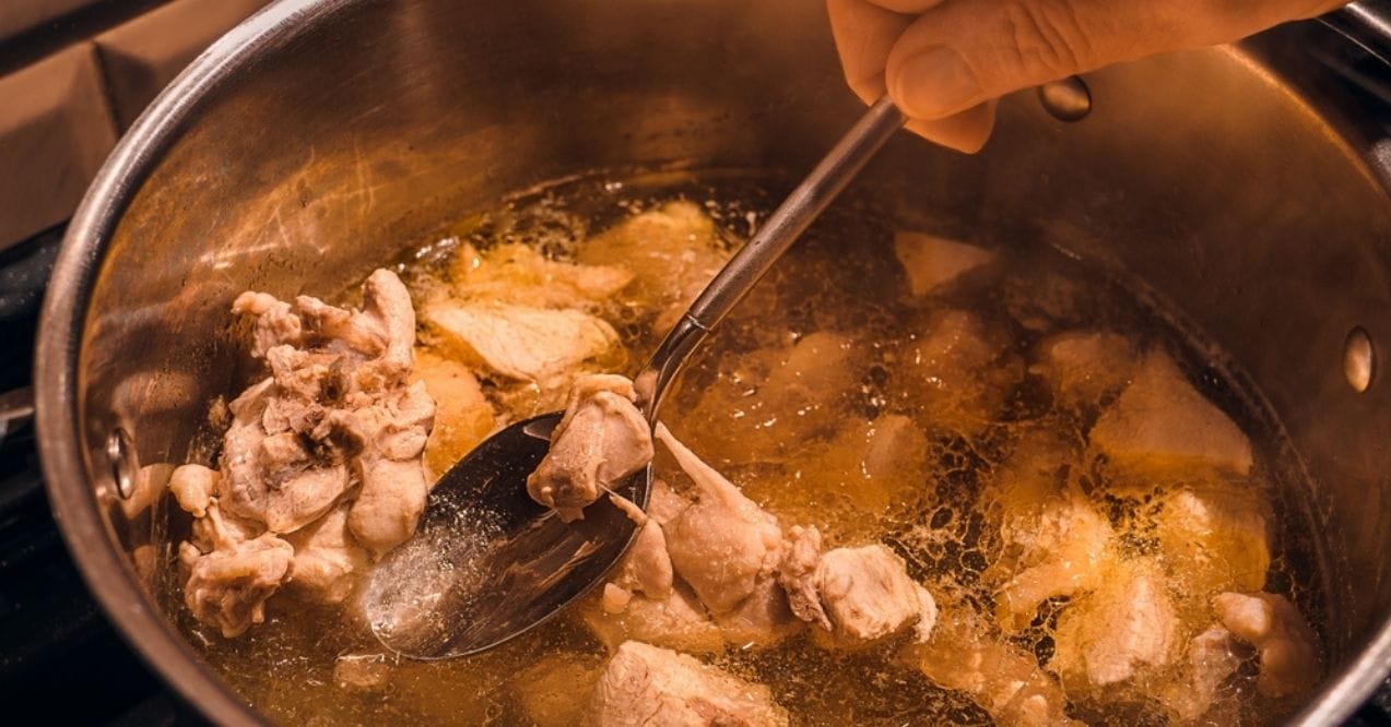 A spoon scooping cooked chicken pieces in broth