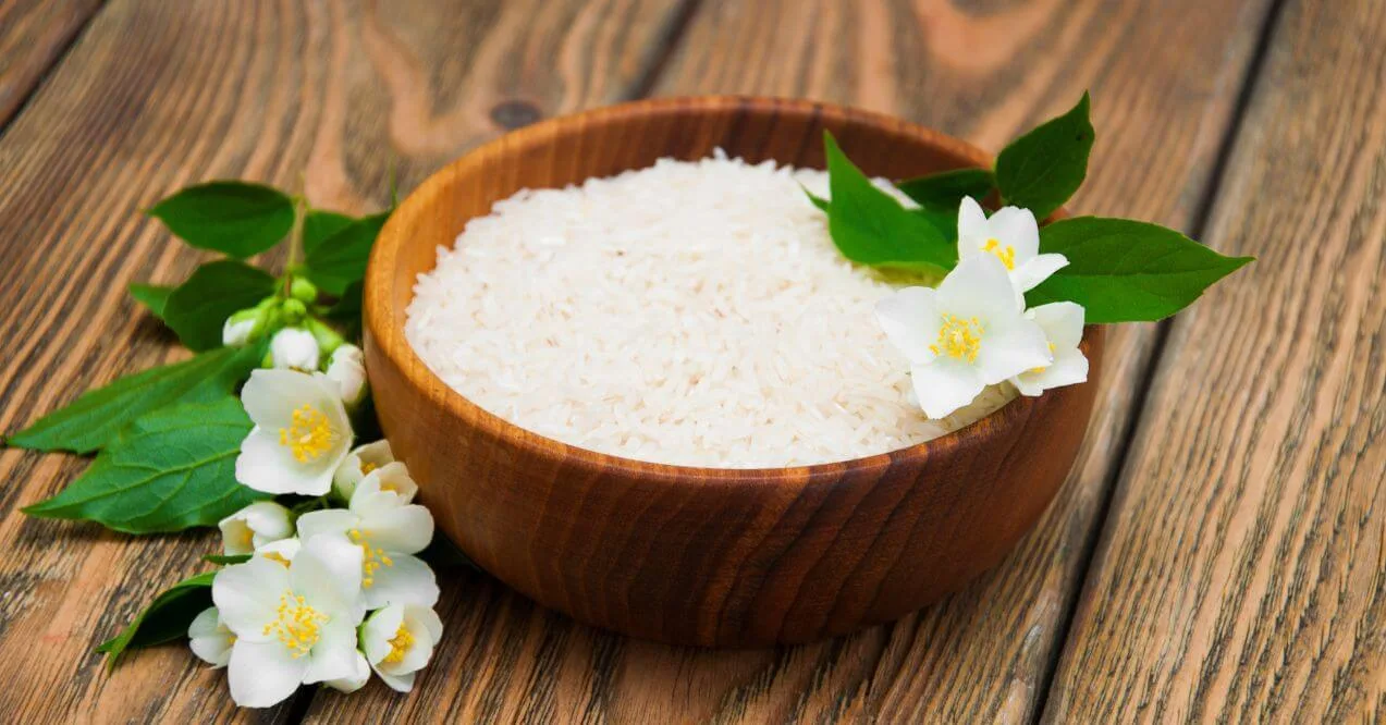 Wooden bowl of jasmine rice with jasmine flowers on a wooden table