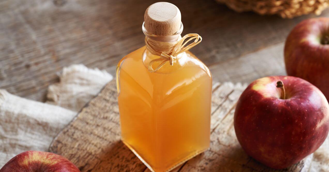 A bottle of apple cider vinegar with apples, a common natural remedy for skin issues.