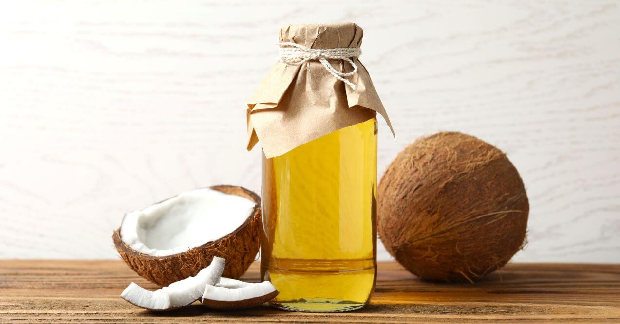 A bottle of coconut oil with coconuts on a wooden table, emphasizing natural remedies for dogs.