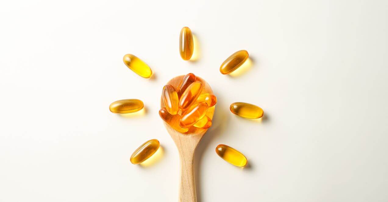 A wooden spoon with omega-3 capsules surrounded by more capsules.