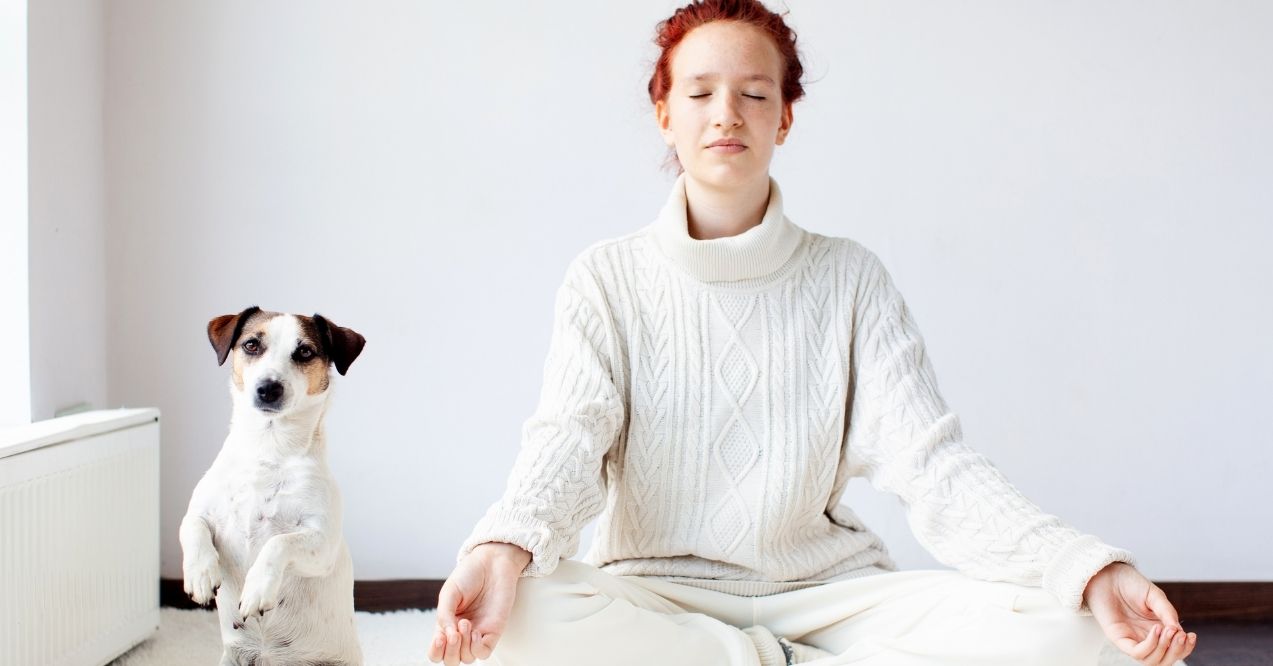 Woman meditating next to a small dog sitting upright on its hind legs